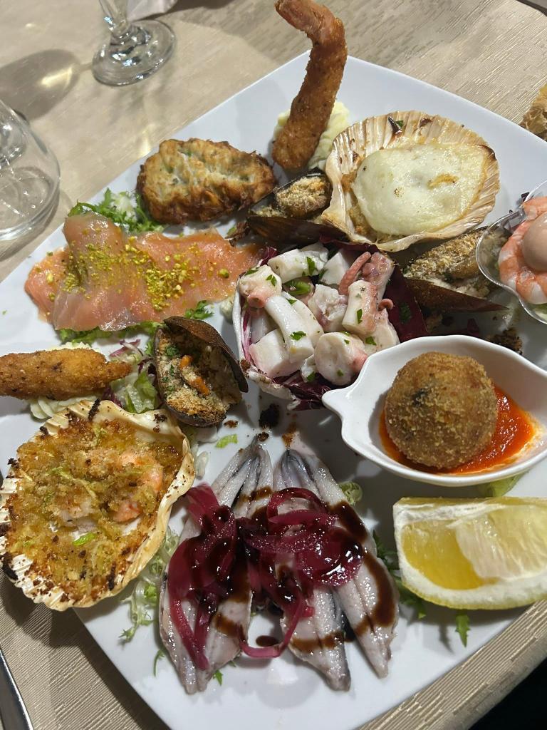 An abundant platter of mixed Italian seafood appetizers including octopus salad, baked scallops, marinated anchovies with red onions, and fried seafood.