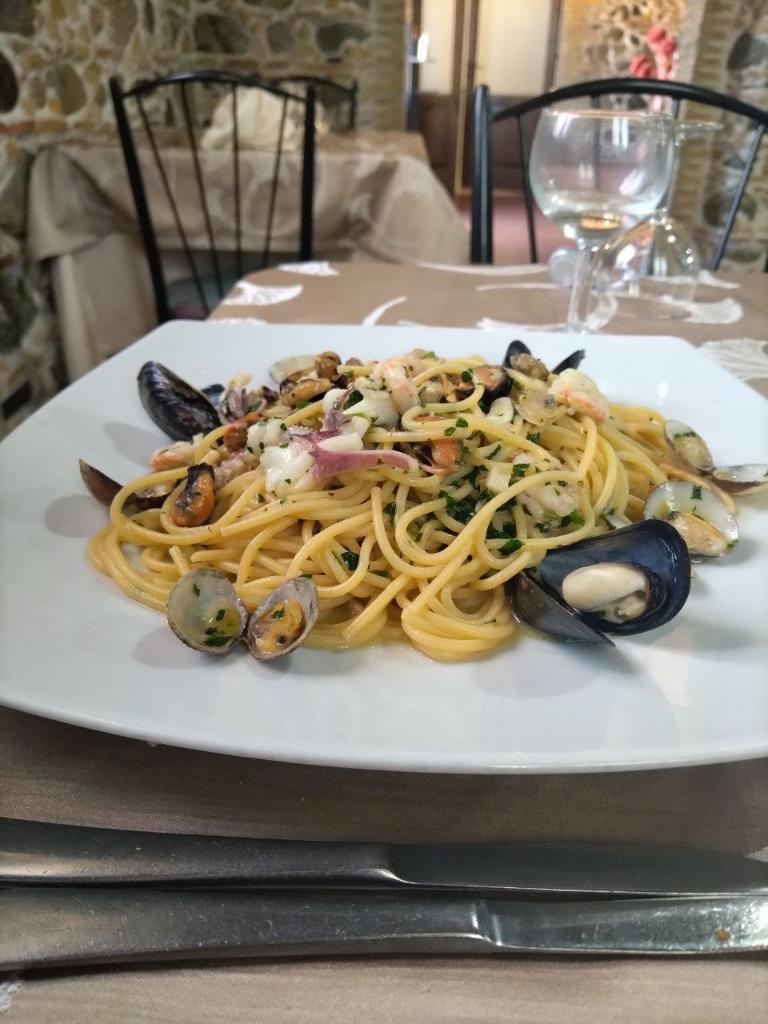 A plate of spaghetti with seafood including mussels, clams, and squid on a rustic restaurant table.